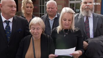 Seis personas frente a un edificio; una mujer rubia lee un documento, acompañada por otras cinco, incluyendo tres hombres y dos mujeres