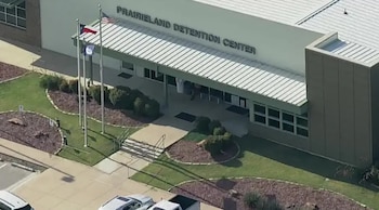 Vista aérea del edificio del Centro de Detención Prairieland con banderas de EE. UU. y Texas. Hay césped, arbustos y autos estacionados