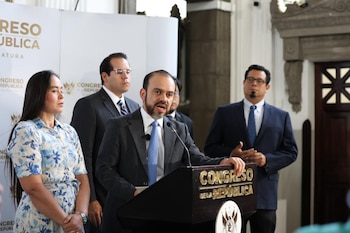 Hombre con barba y traje en podio. Detrás, otros tres hombres con traje y una mujer con vestido. Pancartas del Congreso de la República al fondo