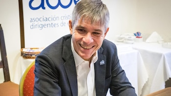 Víctor Valle, hombre de cabello gris y traje oscuro, sonríe. Lleva un pin de ACDE en la solapa. Se ve un cartel de ACDE y mesas al fondo