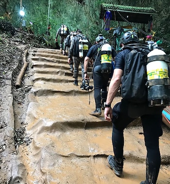 Varias personas equipadas con trajes de neopreno y tanques de oxígeno suben una escalera de tierra embarrada en un entorno natural