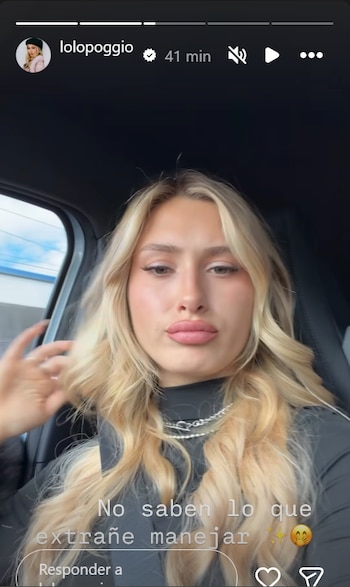 Lolo Poggio sentada dentro de un coche, mirando al frente, con cabello rubio ondulado, vistiendo una camiseta oscura y un collar plateado