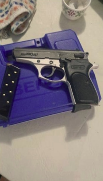 Una pistola negra y plateada sobre un estuche de plástico azul junto a un cargador de municiones