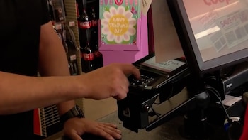 Manos de una persona interactuando con el teclado de una terminal de pago en un mostrador, con una pantalla que muestra opciones de transacción