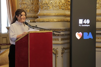 Una mujer habla ante un micrófono en un atril rojo junto a una columna dorada y una pancarta con los logotipos de FIL Guadalajara y BA