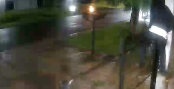 Imagen borrosa de una persona con banda reflectante en la ropa cerca de la entrada de una casa, con alumbrado público en una noche oscura