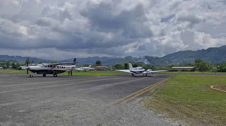 Varias avionetas permanecen sobre la pista de un aeródromo rodeado de vegetación y montañas bajo un cielo nublado. (DGAC)
