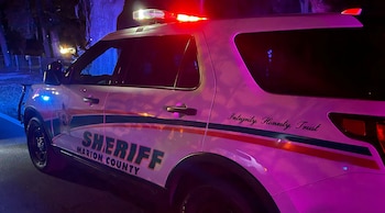 Vista lateral de una patrulla blanca del Sheriff del Condado de Marion con luces rojas y azules intermitentes en la oscuridad de la noche