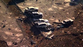 Vista aérea de un aparcamiento con varios vehículos gravemente dañados y escombros dispersos en el suelo oscuro