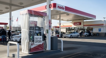 Una gasolinera Nardo con un surtidor de combustible cubierto con plástico y un cartel de "OUT OF ORDER". Varios coches y personas están en la estación.