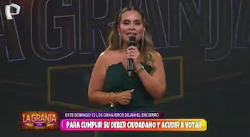 Mujer sonriente con cabello castaño largo y vestido verde esmeralda strapless, sosteniendo un micrófono en un escenario con el logo de 'La Granja' de fondo