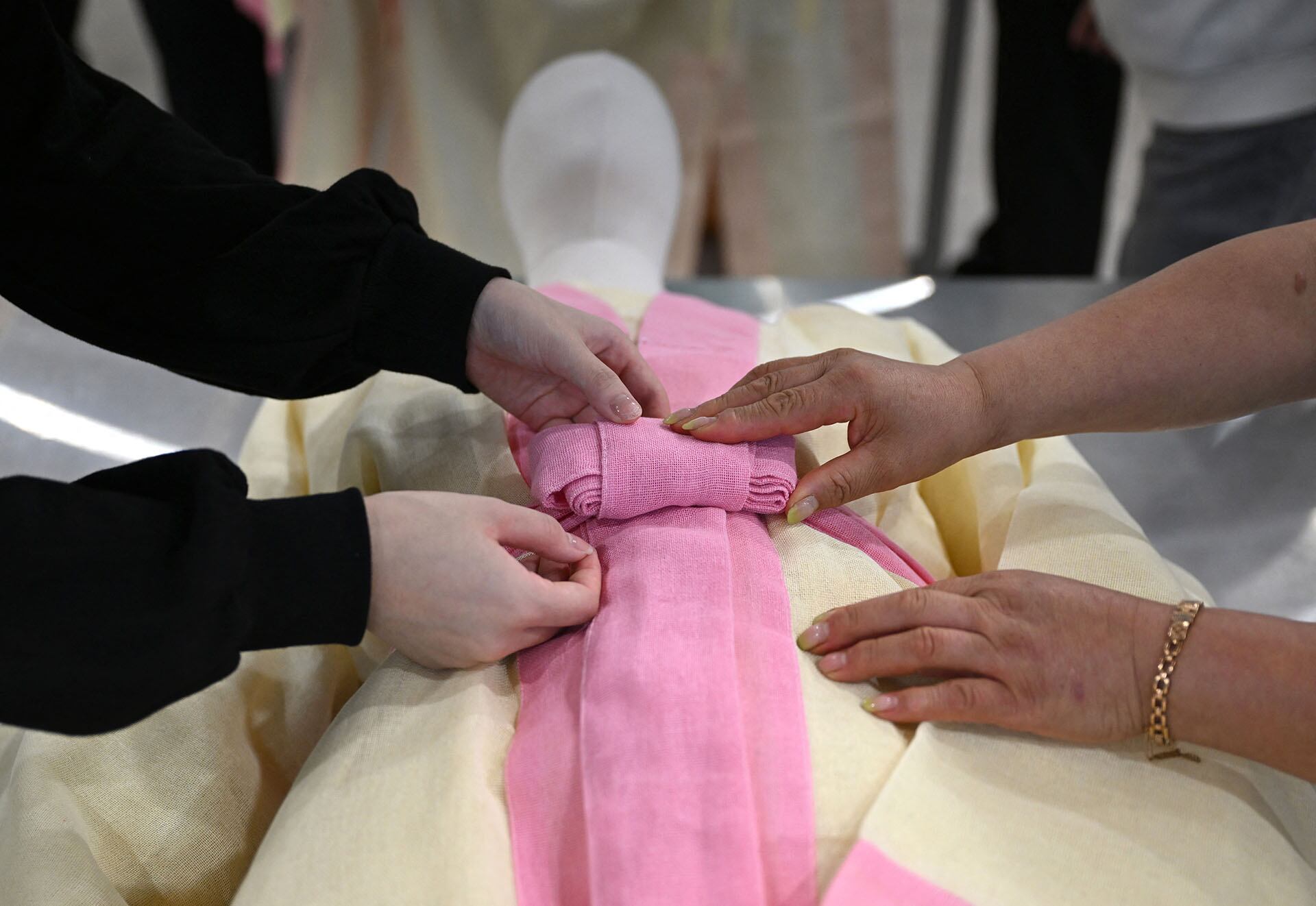 En una fotografía tomada el 24 de septiembre de 2025, estudiantes cubren un maniquí con una tela funeraria tradicional coreana durante una clase de administración funeraria en el Instituto de Ciencia y Tecnología de Busan. (Foto de Jung Yeon-je / AFP)