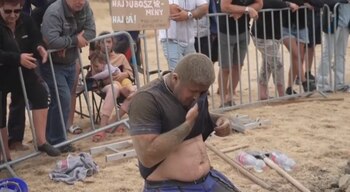 Un hombre sobre la tierra se seca la cara con su camiseta frente a personas detrás de vallas metálicas
