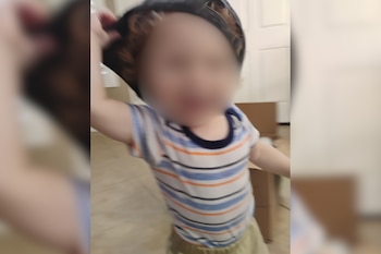 Un niño pequeño con el rostro borroso viste una camiseta a rayas azules, blancas y naranjas, y un sombrero oscuro. El fondo está desenfocado