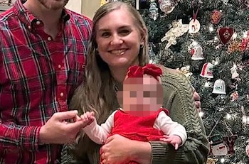 Un hombre y una mujer sostienen a un bebé, todos sonrientes, frente a un árbol de Navidad iluminado y decorado con adornos
