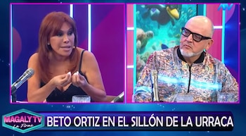 Pantalla dividida con dos presentadores de televisión. Una mujer de pelo cobrizo y un hombre calvo con barba y gafas. Micrófonos y fondos de estudio
