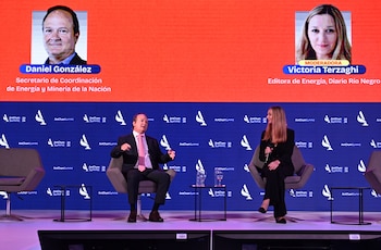 Dos personas sentadas en un escenario durante una conferencia. Detrás, una pantalla muestra sus nombres y títulos: Daniel González y Victoria Terzaghi