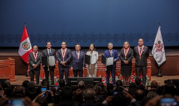Nueve personas en un escenario, con las banderas de Perú y el JNE a los lados. Varios individuos sostienen documentos. Una multitud en la parte inferior