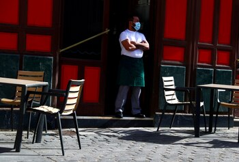 Un mesonero espera la llegada de clientes en una terraza usando un tapabocas