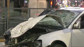 Primer plano de un automóvil blanco con el capó abollado y abierto, y el parabrisas completamente destrozado. Se observan daños severos en la parte delantera