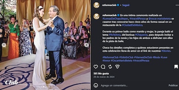 Un hombre con traje azul oscuro y una mujer con vestido blanco de novia bailan tomados de la mano rodeados de invitados