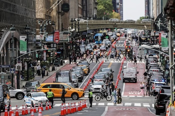 Calle de Nueva York llena de vehículos, incluyendo taxis amarillos y coches de policía, con peatones cruzando una intersección vigilada por agentes