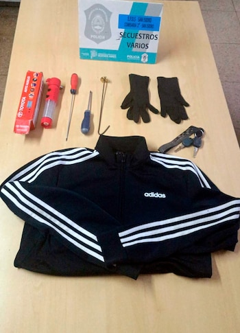 Una campera deportiva negra Adidas, guantes oscuros, dos destornilladores, una linterna roja, una caja de auxilio Toyota y llaves de vehículo