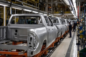 Filas de carrocerías metálicas de camionetas sin pintar colocadas sobre rieles de una línea de ensamblaje industrial.