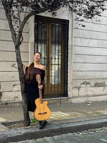 Una persona con cabello largo toca una guitarra acústica con los ojos cerrados frente a un micrófono en un escenario iluminado
