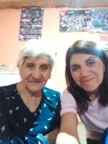 Dos mujeres en un plano cercano miran a la cámara en una habitación con paredes rosas y carteles en el fondo