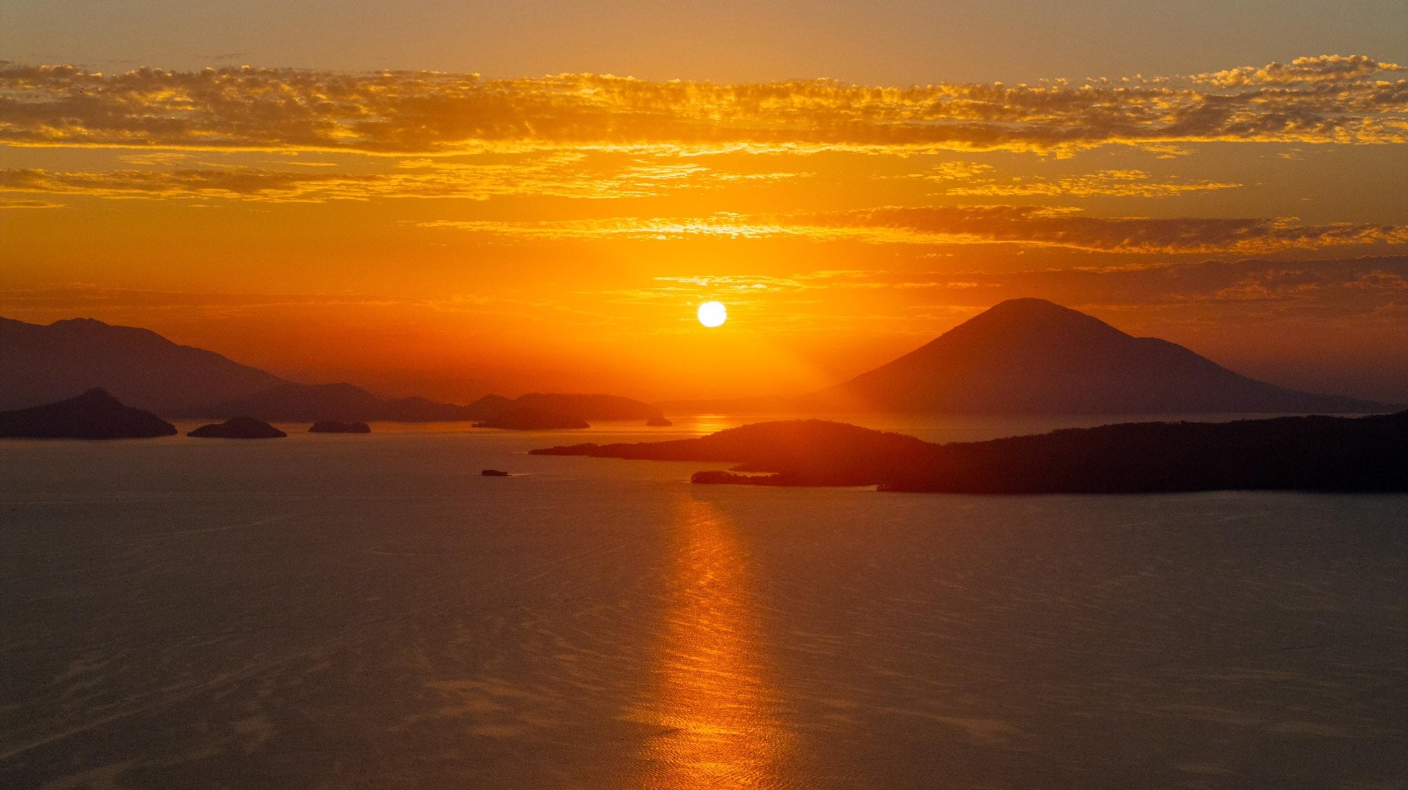 El atardecer pinta de oro y naranja el cielo y la superficie de un lago salpicado de islas y montañas silueteadas.