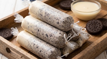 Primer plano de bolis de Oreo envasados en plástico transparente sobre una bandeja de madera, con galletas Oreo y un cuenco de leche condensada al fondo.