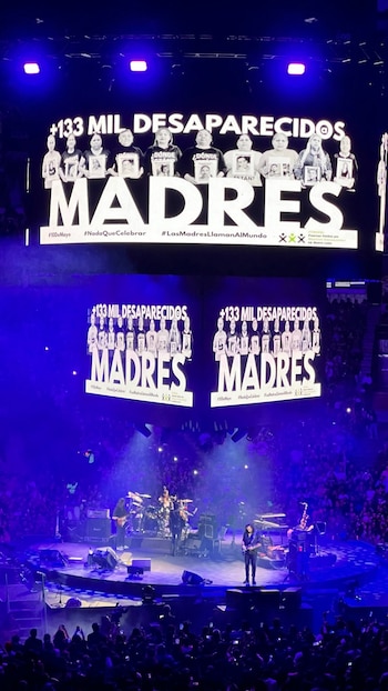 Vista aérea de un concierto donde la banda Caifanes toca en un escenario iluminado. Detrás, pantallas gigantes muestran imágenes de madres y el texto '+133 MIL DESAPARECIDOS MADRES'