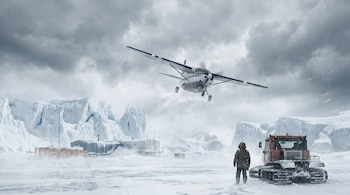 Un avión de hélice desciende sobre un paisaje antártico nevado, con edificios de una estación polar, un vehículo oruga y una persona con parka.