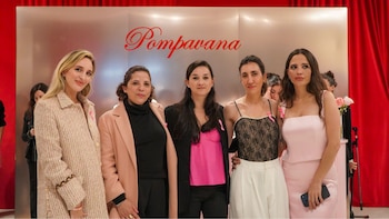 Cinco mujeres posan alineadas frente a un panel metálico con el nombre Pompavana escrito en rojo y cortinas rojas a los lados