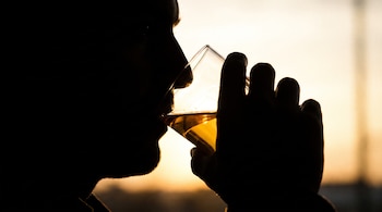 Silueta de un hombre llevando un vaso con un líquido dorado a su boca, con un fondo luminoso