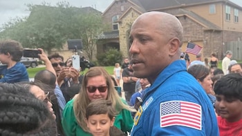 Hombre de tez oscura con traje azul de uniforme y parche de la bandera estadounidense en el hombro derecho, rodeado por una multitud que toma fotos con teléfonos