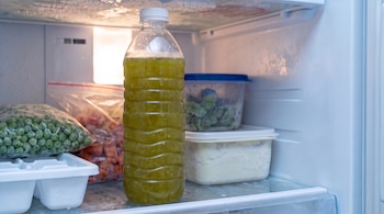 Botella de plástico con tapa blanca y líquido verde dentro de un congelador junto a bolsas de guisantes y recipientes de comida.