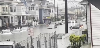 Una calle de zona residencial cubierta por agua acumulada con automóviles parcialmente sumergidos frente a casas