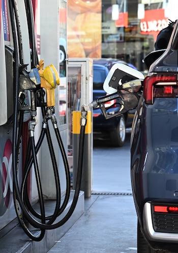 Vista detallada de un coche azul oscuro siendo repostado en una gasolinera, con la boquilla de la manguera de combustible insertada en el tanque
