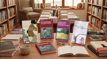 Una mesa de madera con cuatro libros de Yiyun Li en exposición, libros apilados, una taza de café, gafas, una planta suculenta y estanterías llenas de libros.