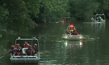 Tres botes con personal de rescate navegan en un río bordeado por vegetación densa. Los botes tienen luces de emergencia encendidas