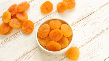 Albaricoques deshidratados de color naranja ubicados dentro de un tazón blanco y sobre una superficie de madera blanca.