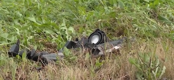 Restos plásticos negros de un faro de vehículo tirados entre la hierba verde y la vegetación seca