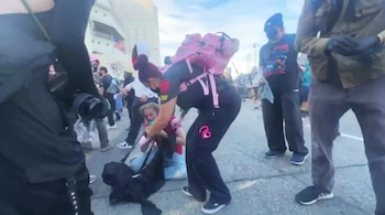 Un manifestante universitario con sangre en el ojo es asistido por una persona con mochila rosa en el suelo de una calle durante una protesta