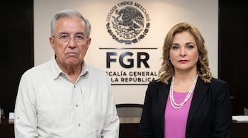 Un hombre y una mujer de pie frente al logo de la Fiscalía General de la República de México. El hombre lleva camisa clara, la mujer blazer oscuro y collar de perlas.