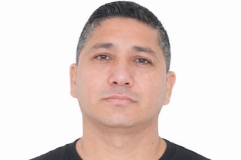 Primer plano del rostro de un hombre con cabello oscuro y canas, piel clara y ojos marrones, vistiendo una camiseta negra, sobre fondo blanco.