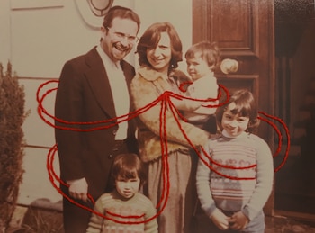 Una fotografía sepia de un hombre, una mujer, un bebé, una niña y un niño. Hilos rojos bordados trazan líneas alrededor y entre las figuras