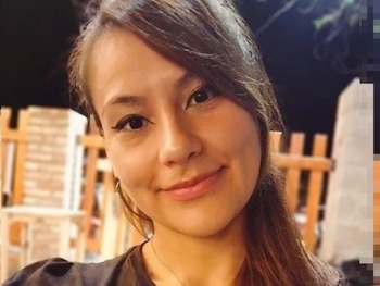 Primer plano de Shadya Altamirano, mujer joven con cabello castaño, sonriendo sutilmente, fondo borroso con estructuras de madera