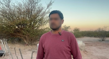 Hombre con un suéter granate y el rostro borroso frente a vegetación seca y suelo de tierra